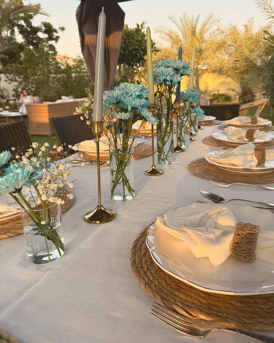 A long garden table with blue flowers, gold candlesticks and rope placemats