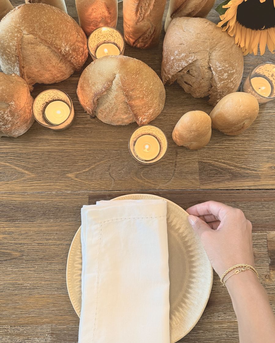 Hands placing a linen napkin beside loaves of bread, sunflowers and candlelight