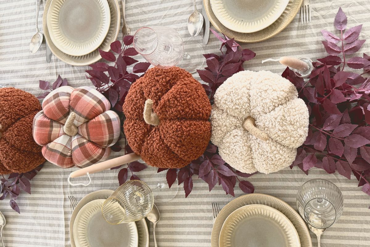Soft knitted pumpkins and plum-coloured leaves along a striped tablecloth