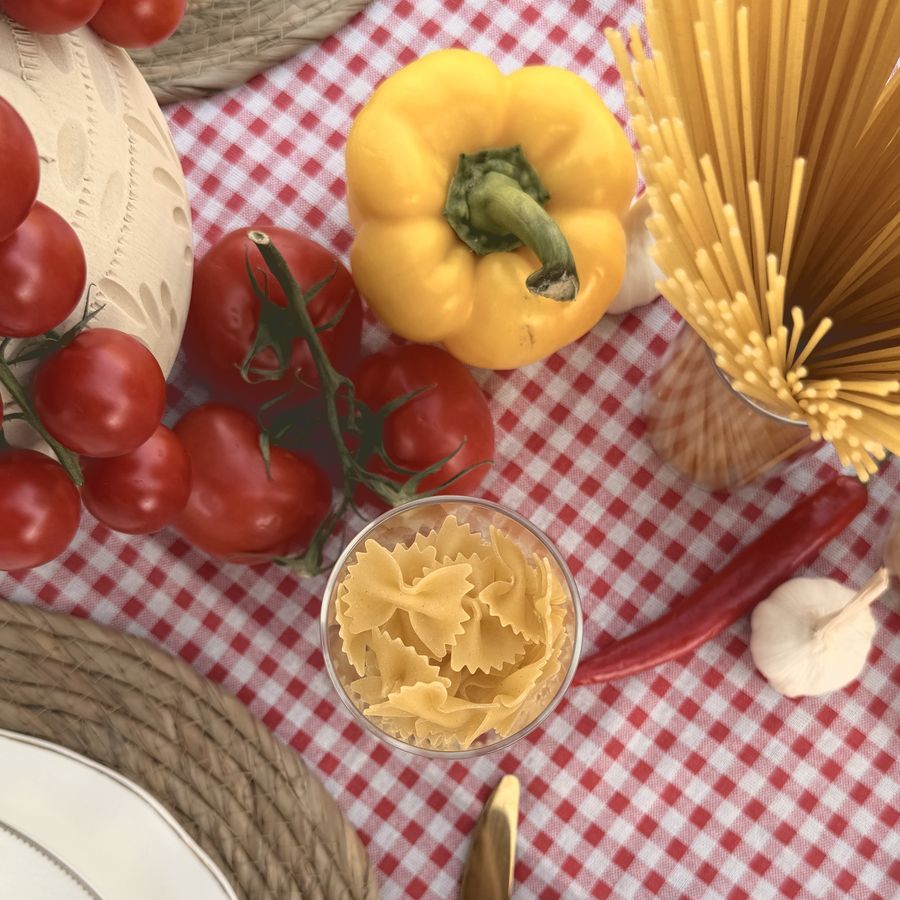 Cherry tomatoes, a yellow pepper and dried pasta on a red gingham cloth