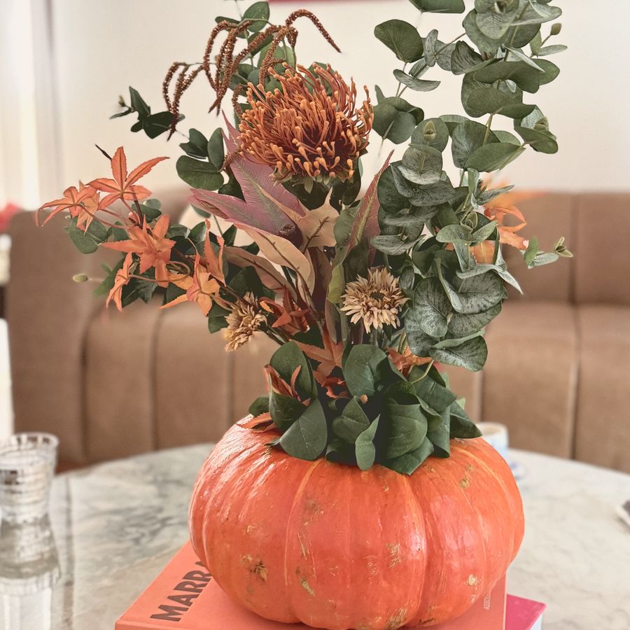A floral pumpkin with eucalyptus and protea sitting on a stack of books