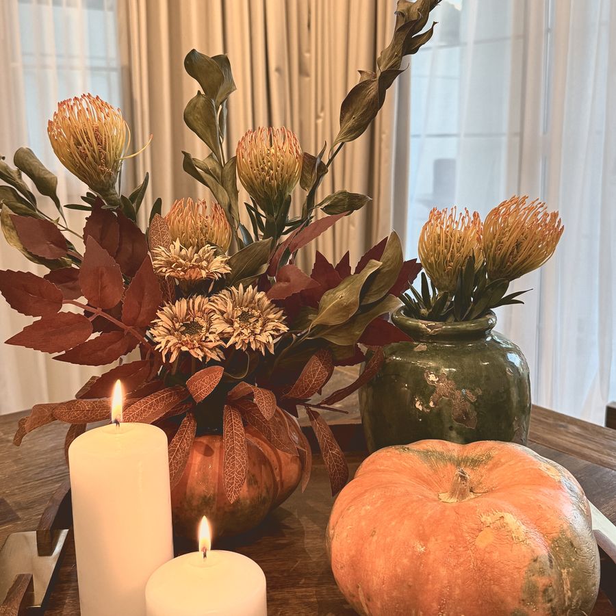 An autumn centrepiece with proteas, a pumpkin and candles on a wooden tray